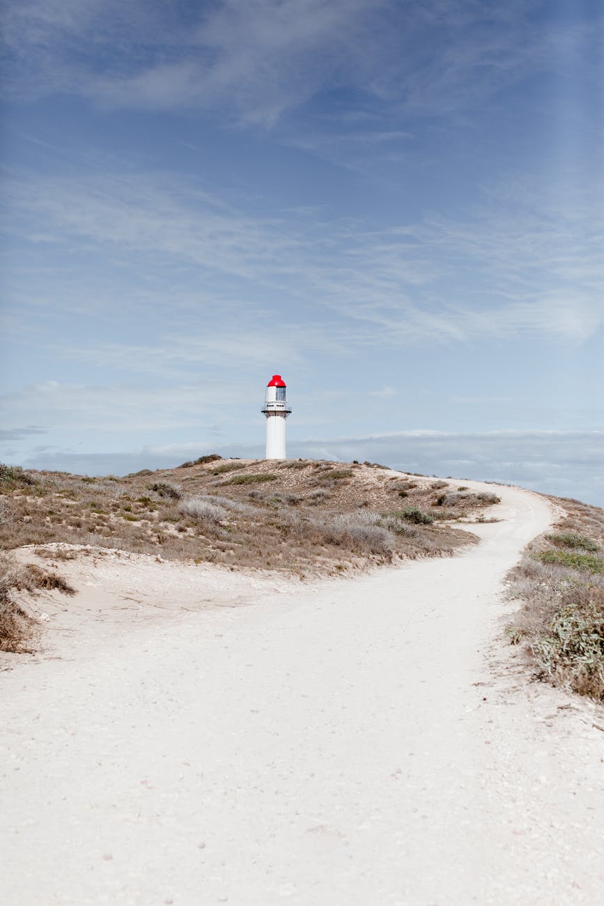 lighthouse on shore against sea under cloudy sky