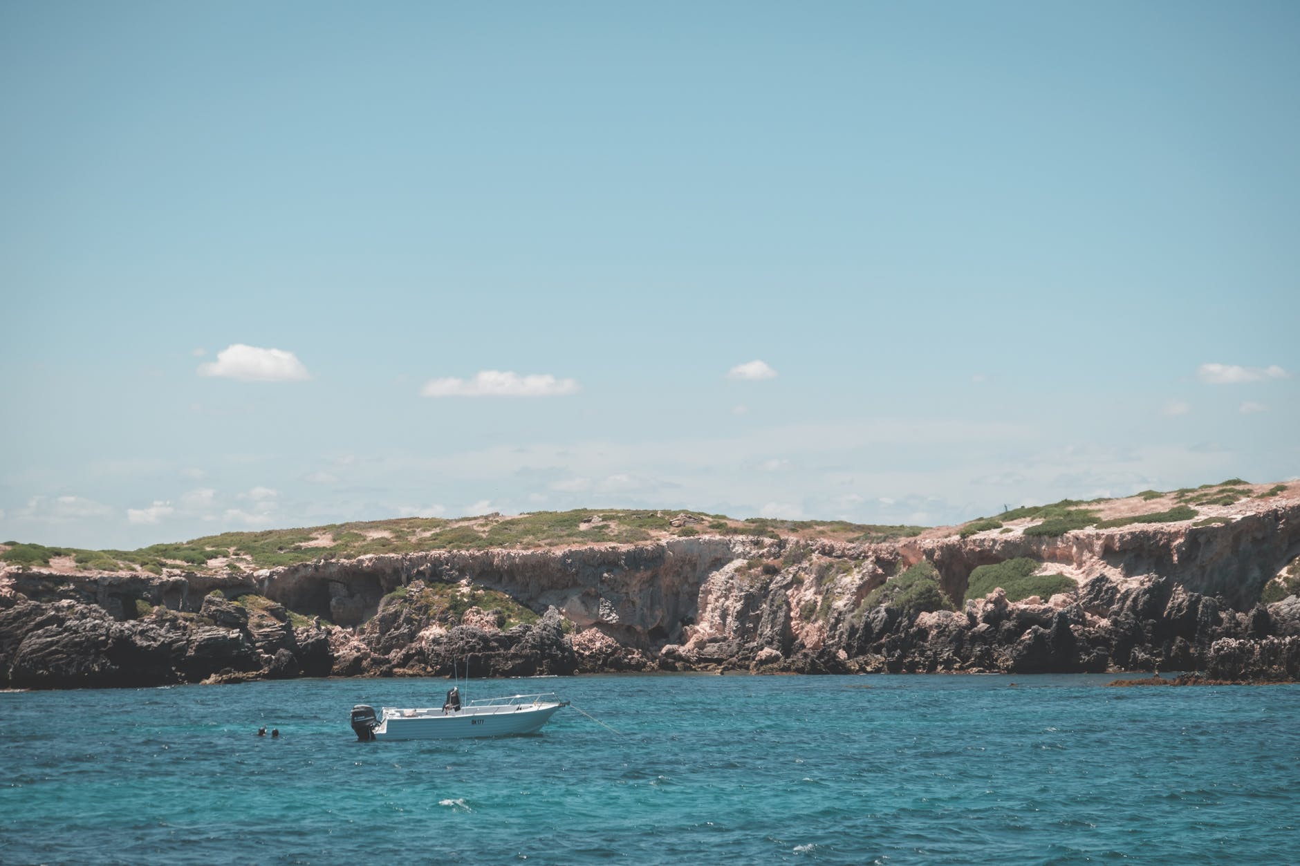 boat floating on sea near rocky island under blue sky