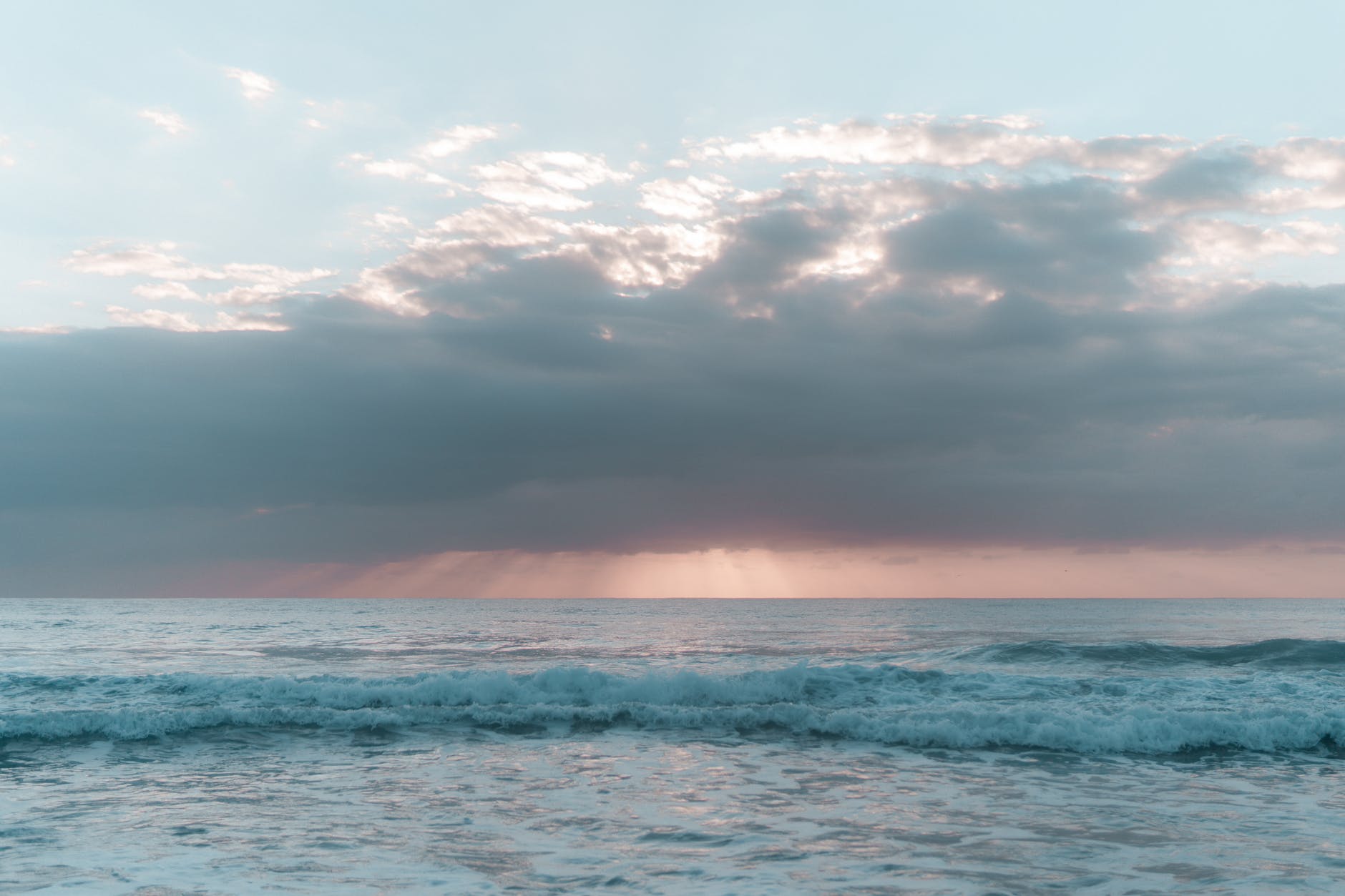 foamy ocean under cloudy sky at sunset